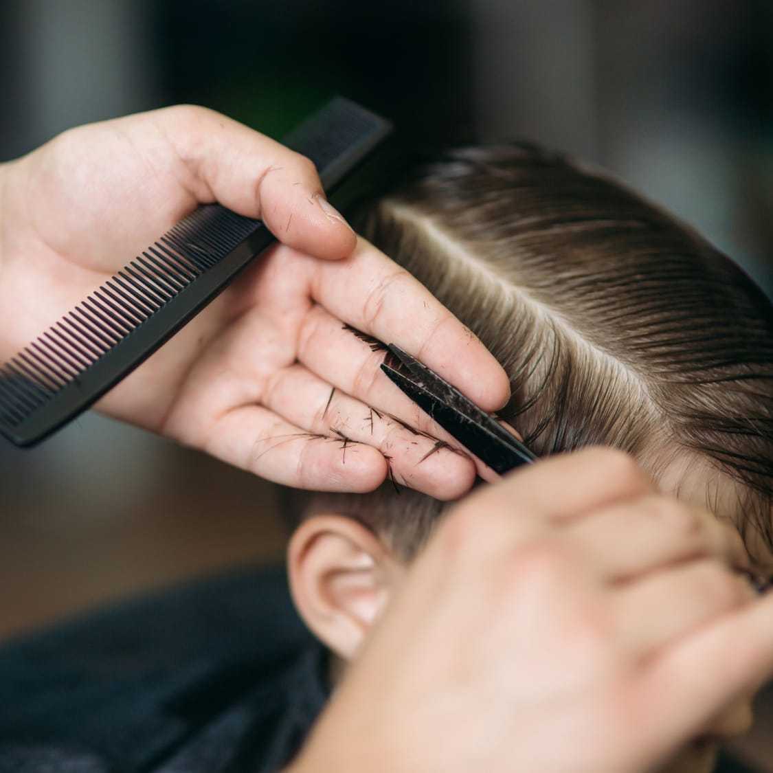 A hairstylist cutting a person's hair with scissors and a comb.