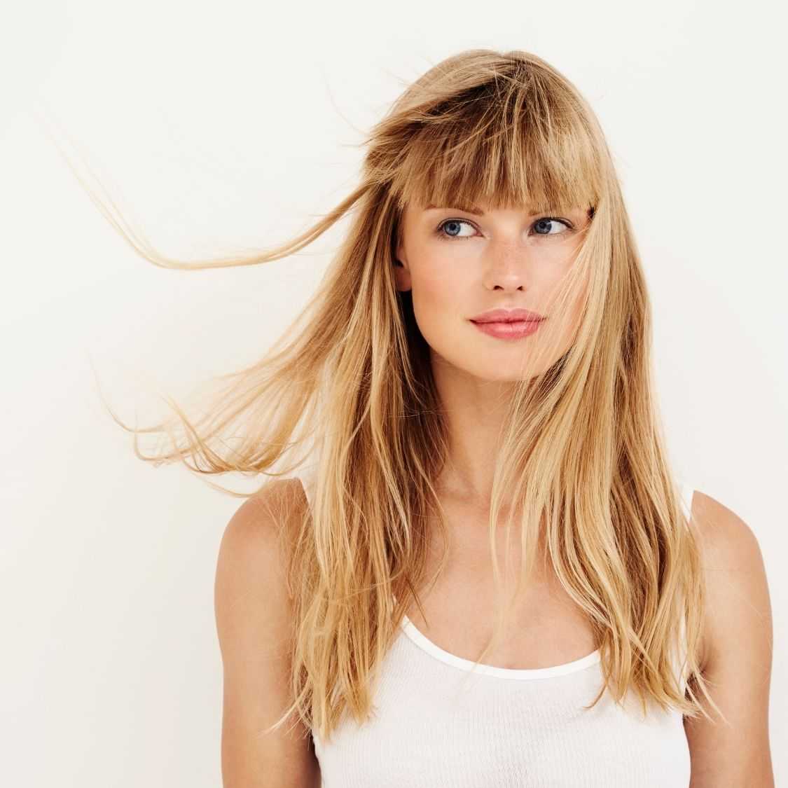 Woman with blond hair and bangs, wind-blown hair, white tank top.