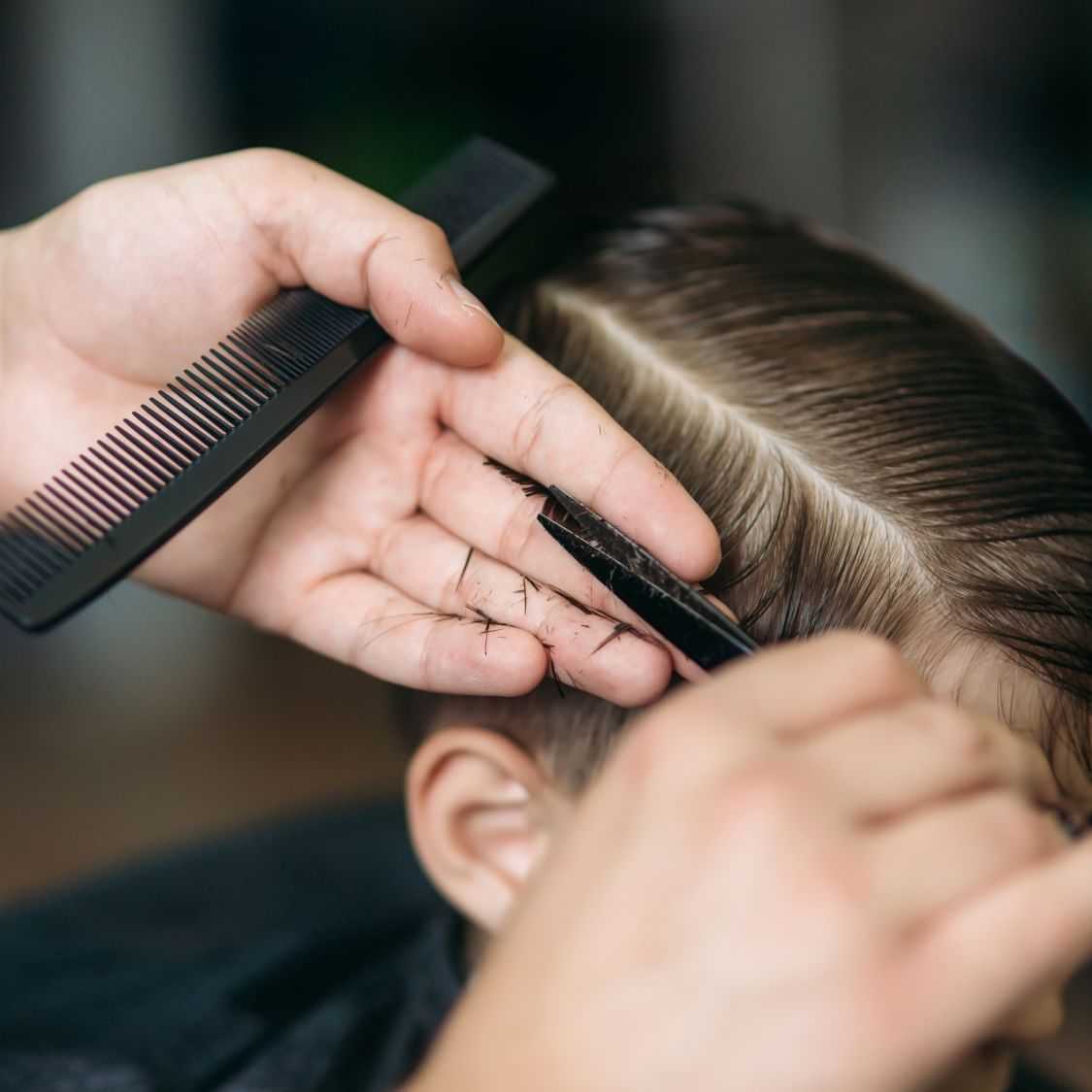 A hairstylist cutting a person's hair with scissors and a comb.